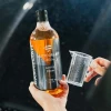 Ręka trzyma butelkę CARNELIAN Active Foam obok miarki, w tle rozmyty samochód nocą