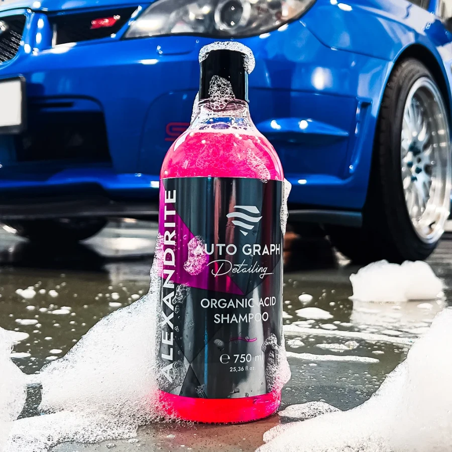Butelka ALEXANDRITE Organic Acid Shampoo z pianą na zakrętce, na mokrej posadzce przy niebieskim aucie