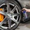Dłoń spryskuje AMETHYST Rim Cleaner na aluminiową felgę z pomarańczowym zaciskiem hamulcowym
