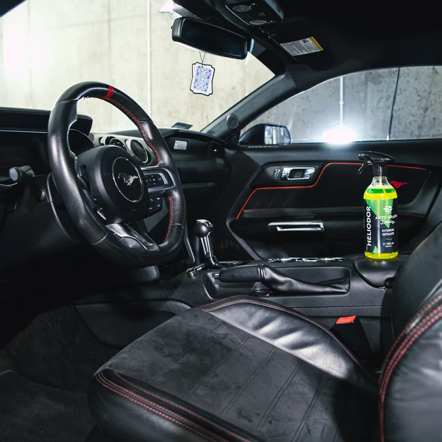 Butelka HELIODOR Interior Detailer na konsoli w sportowym wnętrzu auta z czerwonymi przeszyciami