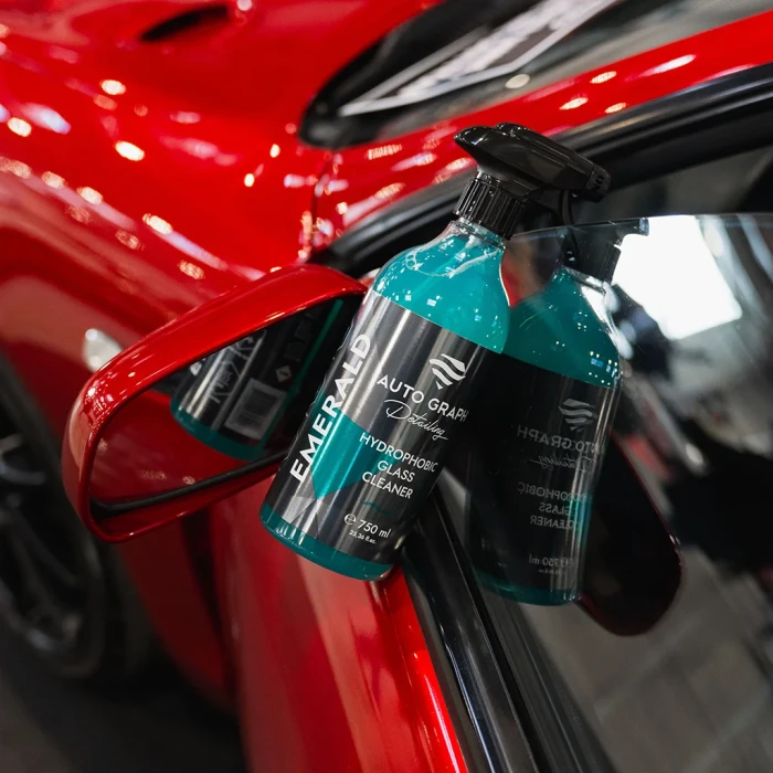 butelka EMERALD Hydrophobic Glass Cleaner zawieszona przy lusterku bocznym czerwonego samochodu