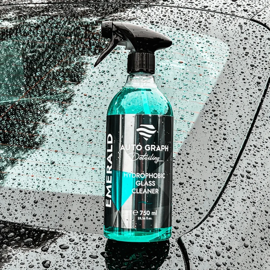 butelka EMERALD Hydrophobic Glass Cleaner stojąca na masce samochodu pokrytej kroplami deszczu