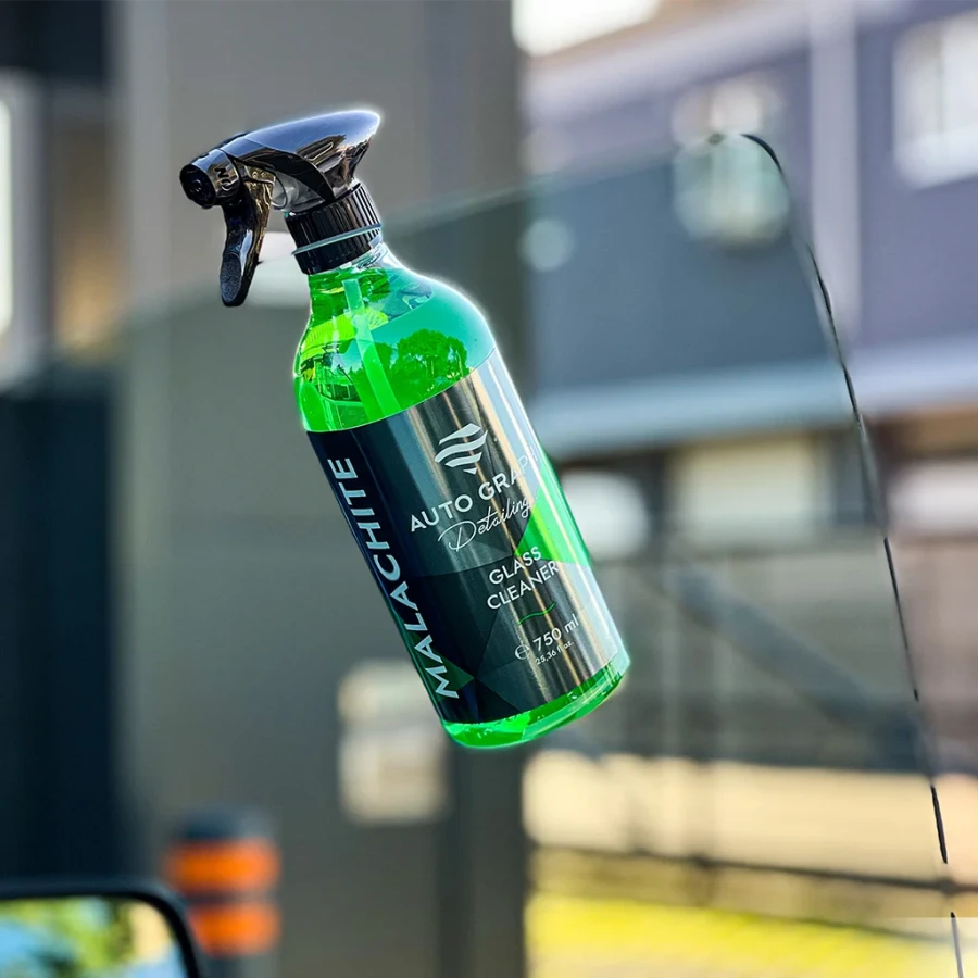 butelka z atomizerem MALACHITE Glass Cleaner przy szybie samochodu na tle rozmytej zabudowy