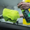 dłoń spryskuje szybę samochodu MALACHITE Glass Cleaner i przeciera ją zieloną ściereczką z mikrofibry